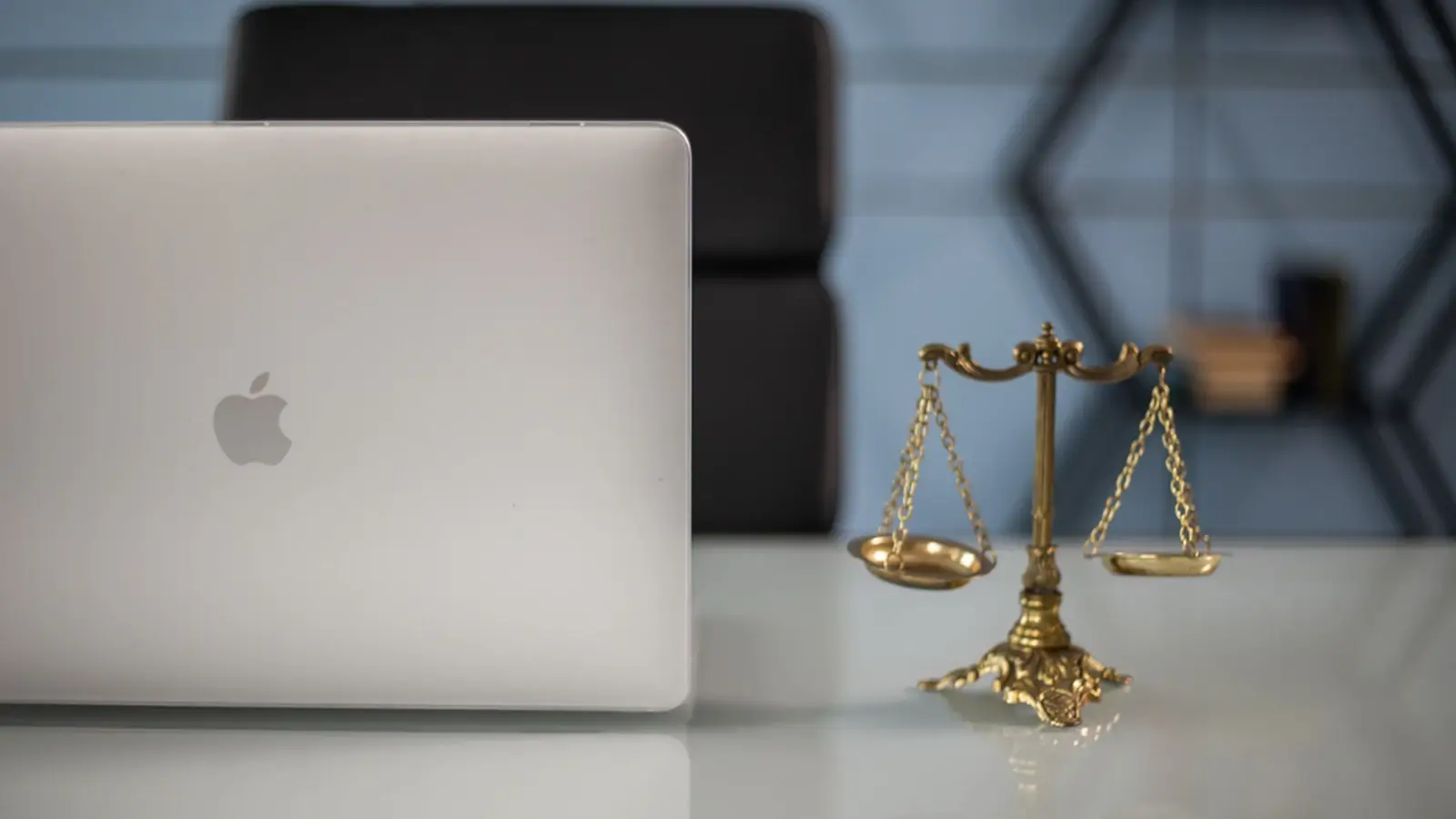 A justice scale beside a laptop on an office desk, representing legal and administrative services.