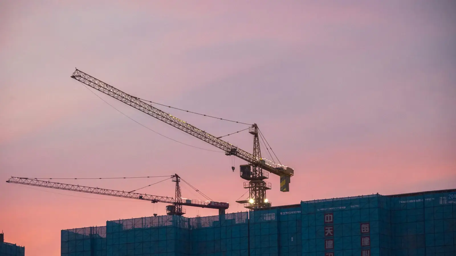 Construction cranes above a building site at sunset, representing construction and trade services.